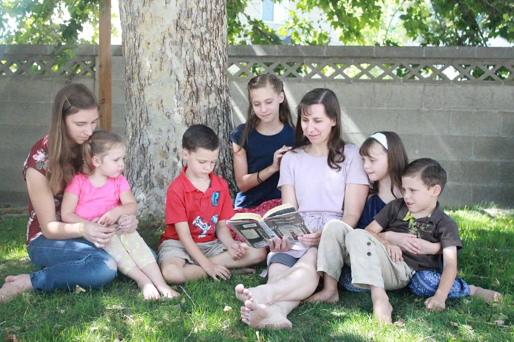 mom reading to 6 children under a tree