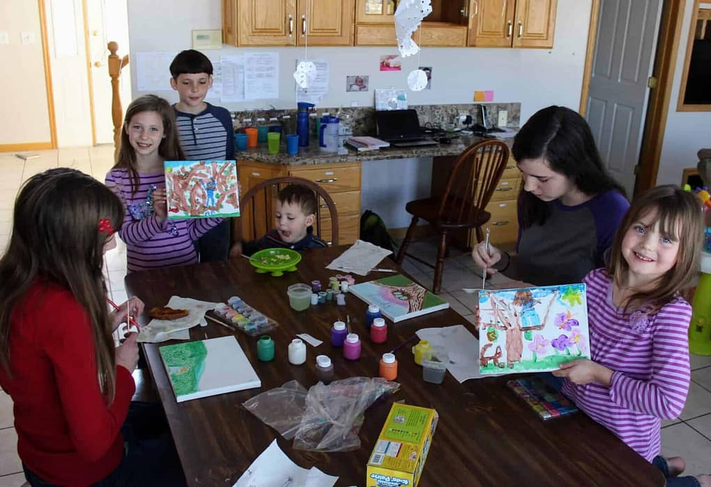 6 children doing painting canvas art projects at the kitchen table