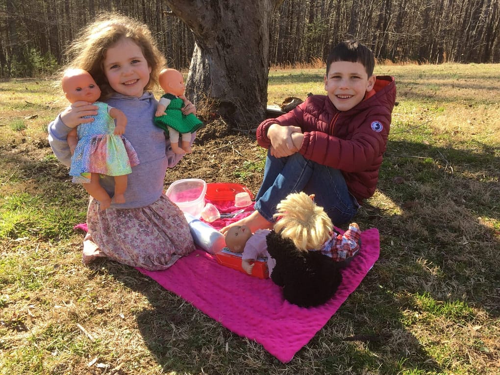 two little siblings playing outside and having a picnic with their dolls together on a sunny winter day