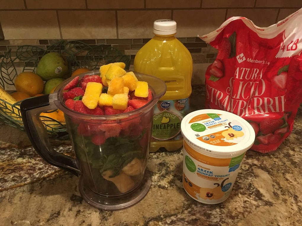 blender full of smoothie ingredients not yet blended. mango, strawberry, kale, banana, yogurt