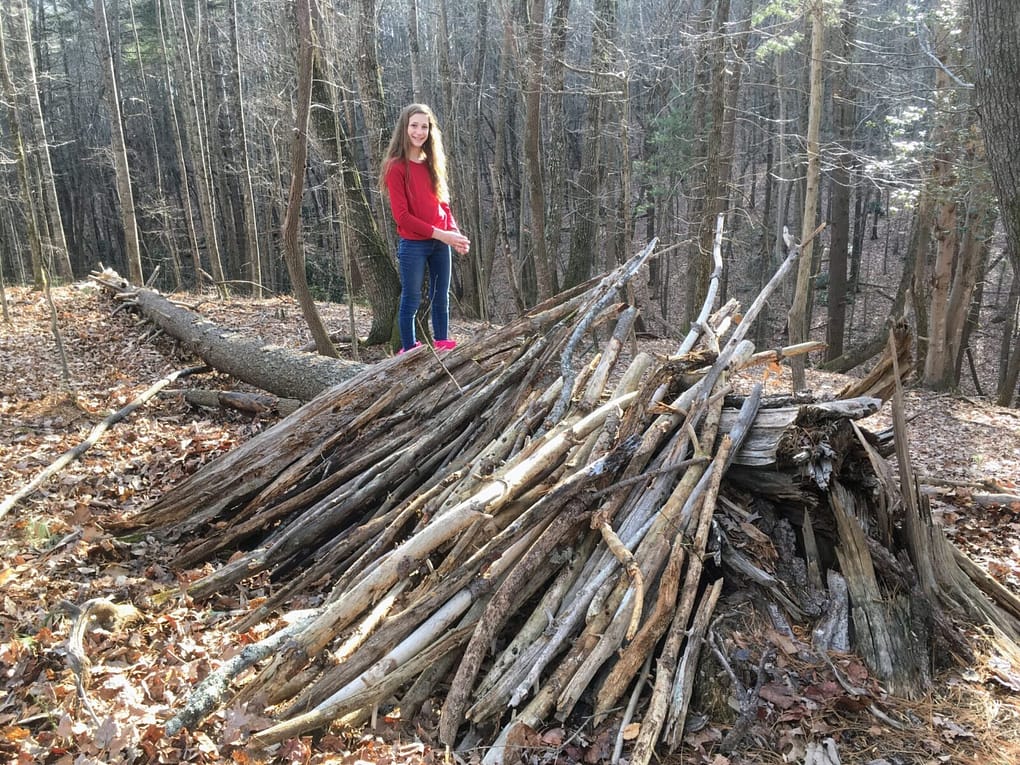 Girl builds a fort with large branches at nature school