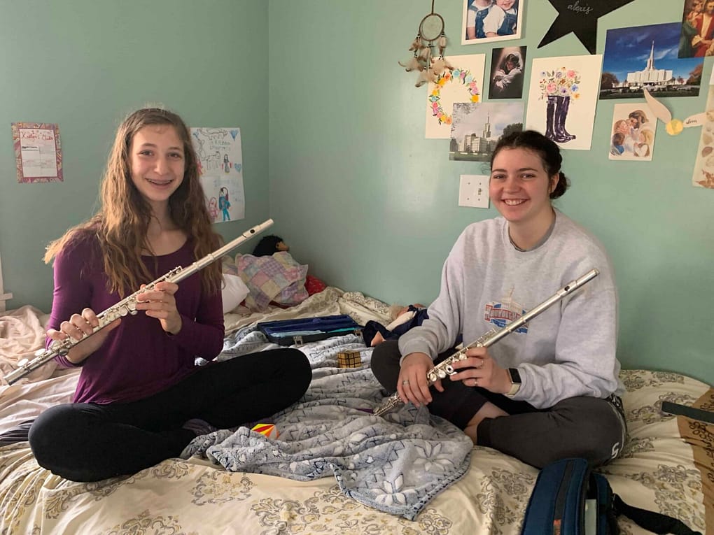 two sisters sitting on their bed playing the flute
