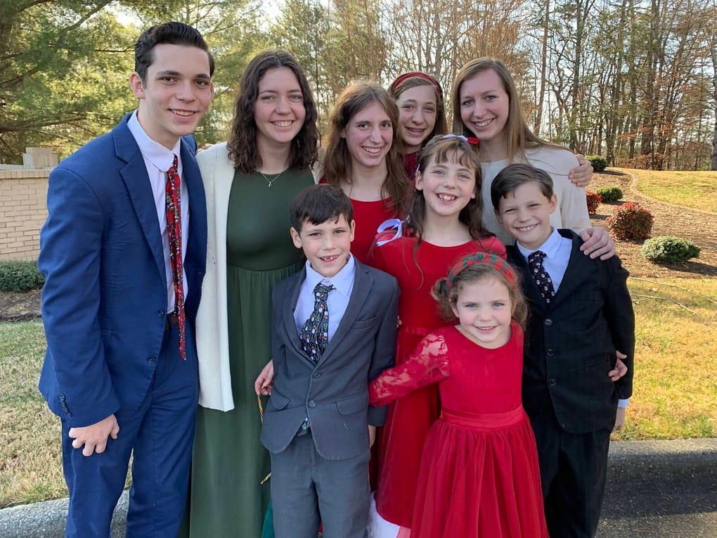 9 children dressed in Christmas colors Sunday best clothes hug and pose for Christmas Eve picture outside after church