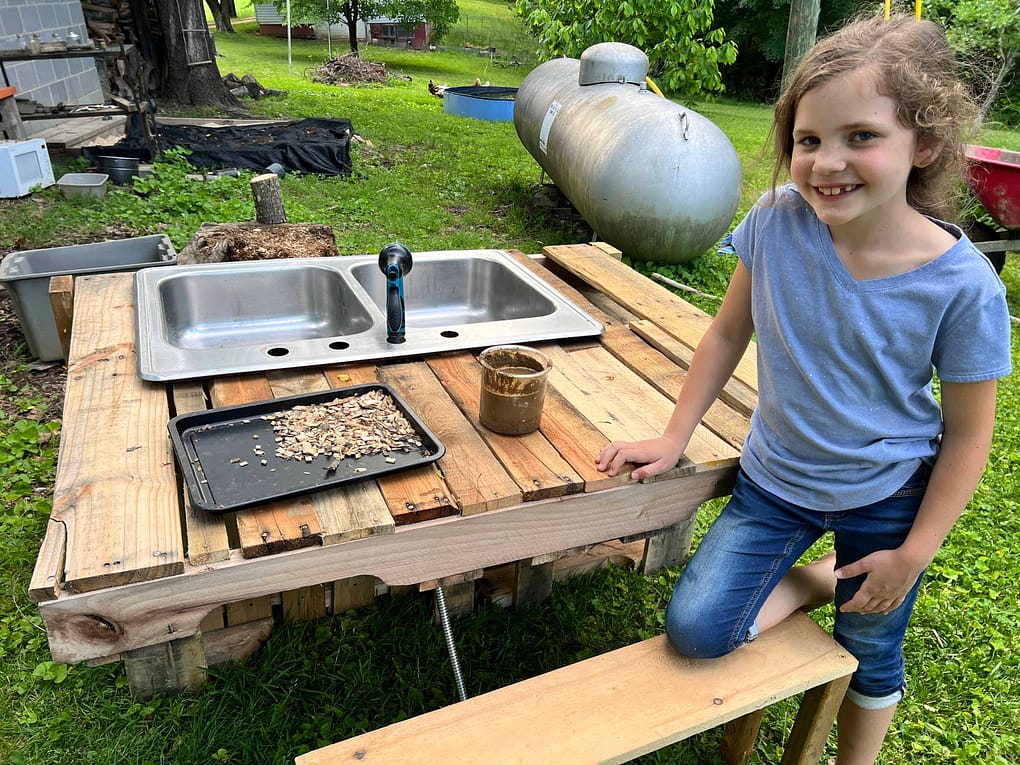 7 year old girl standing next to her mud kitchen sink