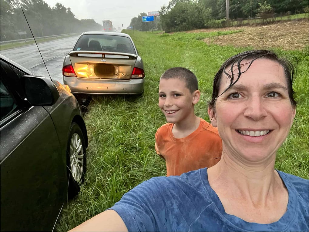 mom and son with broken down car in the rain