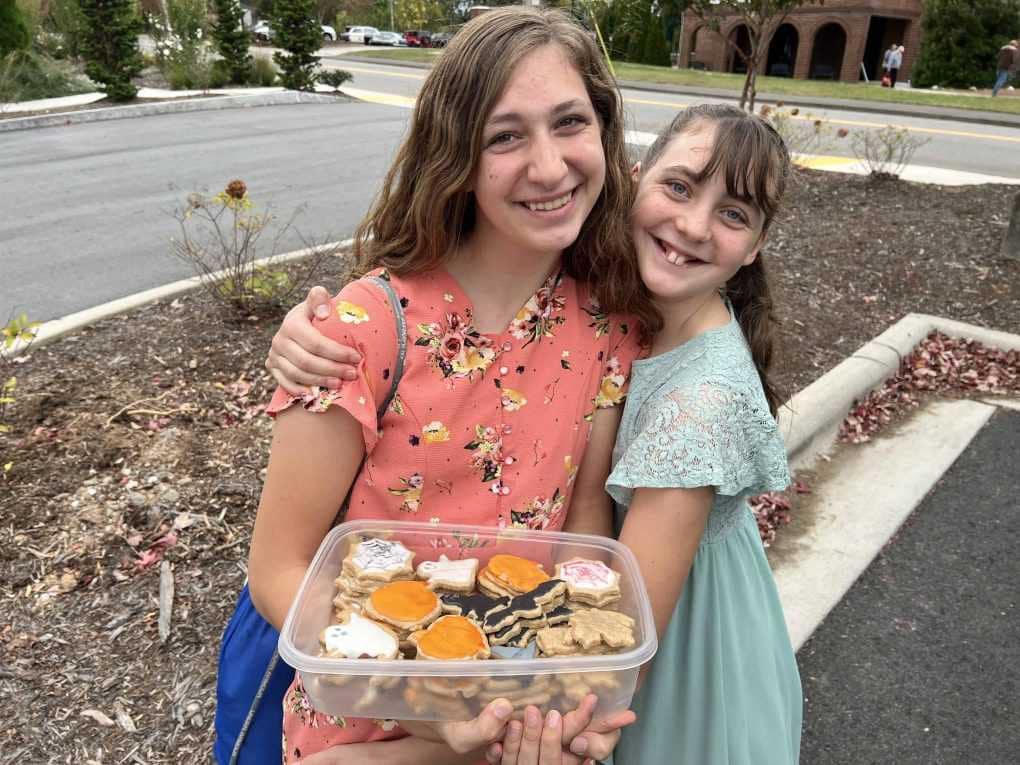 sisters hugging with a container of cookies