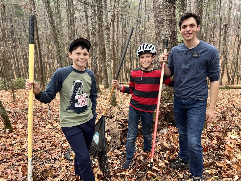 3 boys holding rakes in the woods