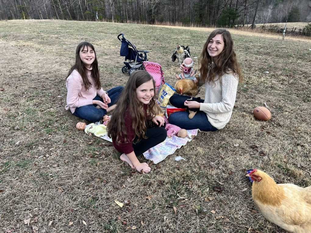 3 sisters eating a picnic with dolls in winter
