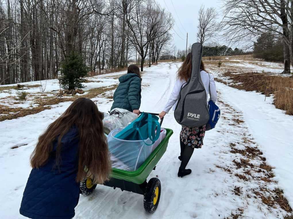 kids taking a John Deere poly cart full of stuff up a road in the snow