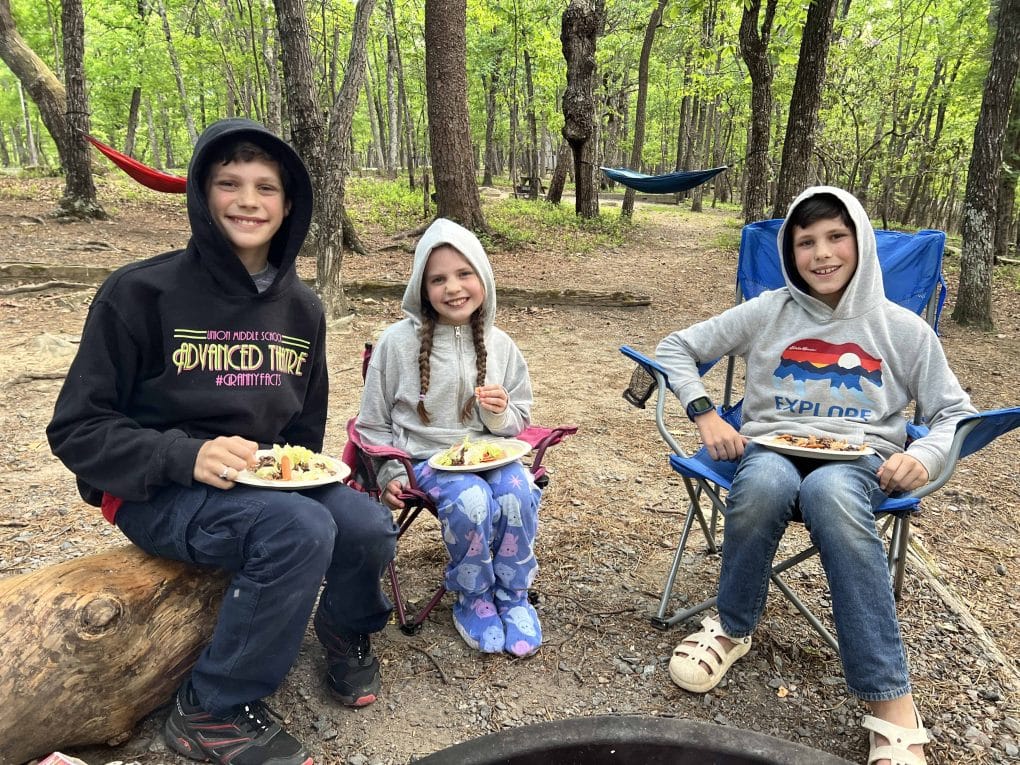 3 kids eating dinner at a campground