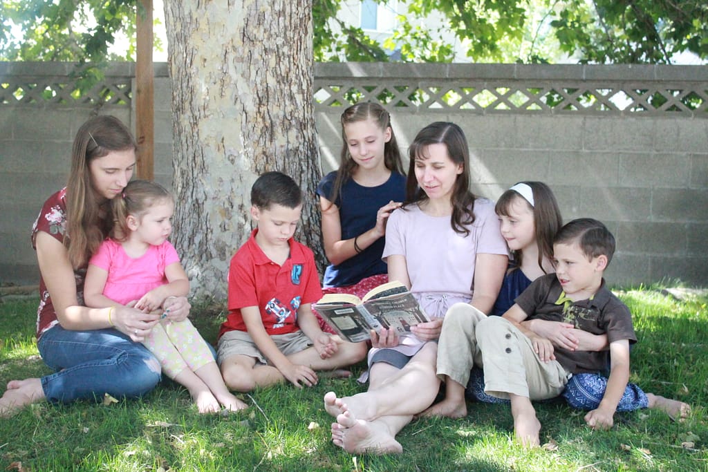 a mother reads out loud to her children under a big tree.