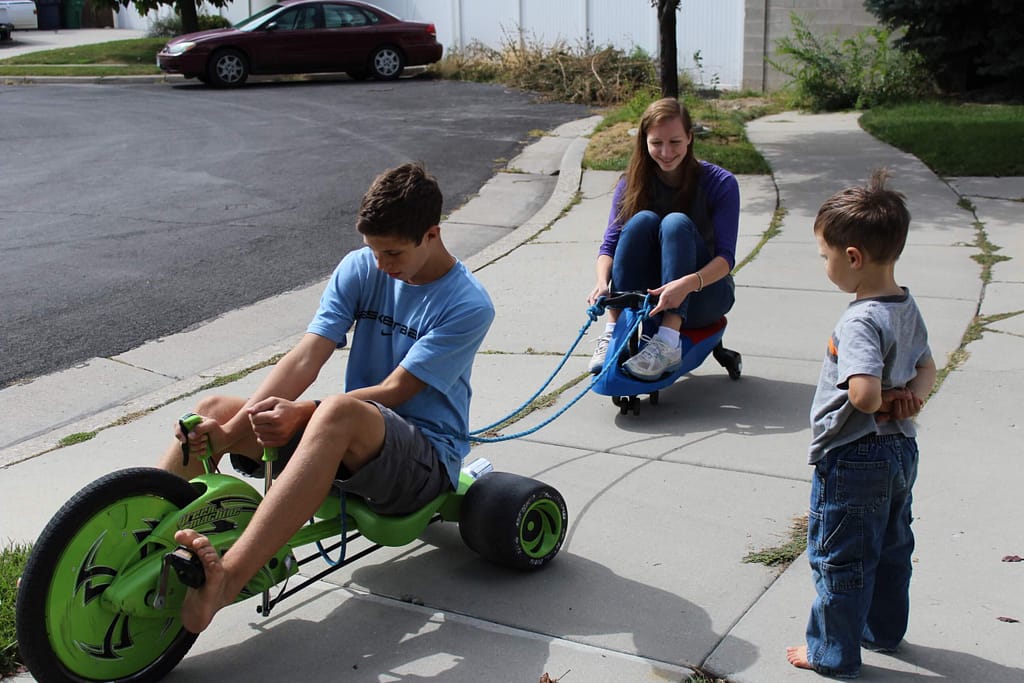 teen brother on a green machine bike pulls teen sister on a plasma car for a fun PE activity.