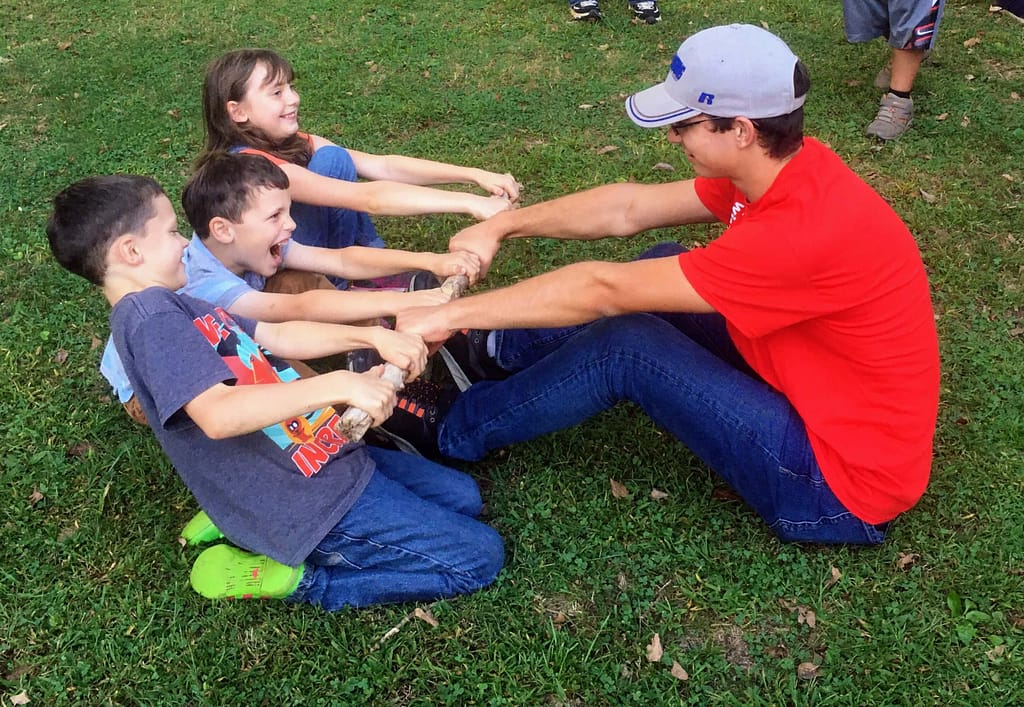 boys play stickpull. Three kids on one side against 1 teenage boy on the other side.