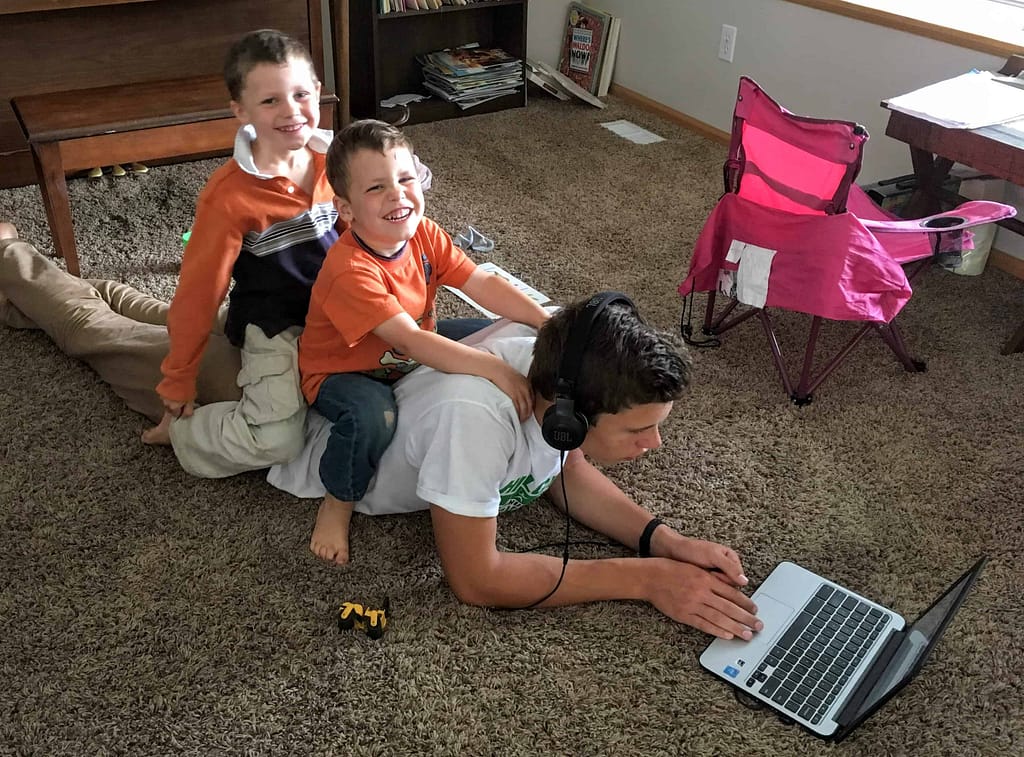 teen boy on computer with 2 little brothers sitting on his back