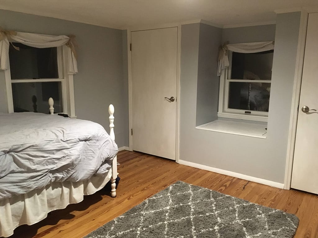master bedroom with a gray comforter, Moroccan shag rug, swag valances with burlap ties, window seat.