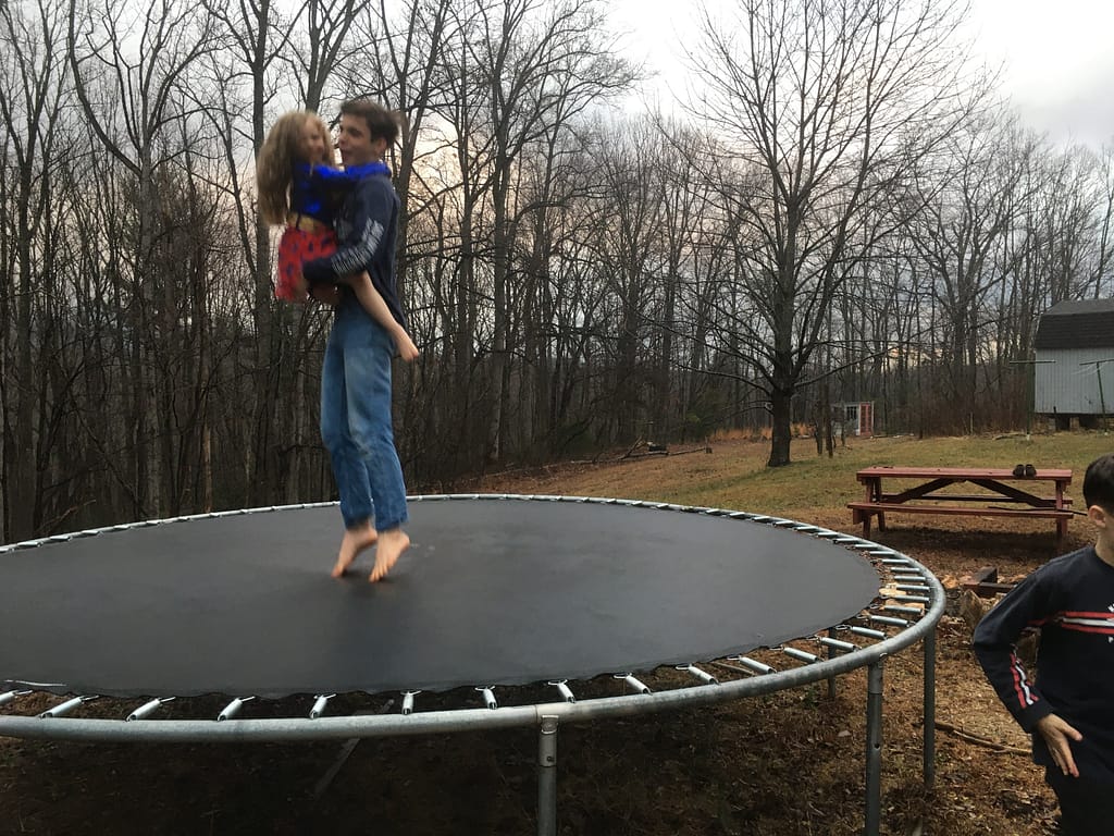 big brother holding little sister and jumping on the trampoline in winter