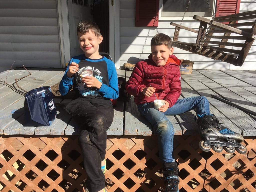 Two brothers playing outside and eating their lunch on the porch