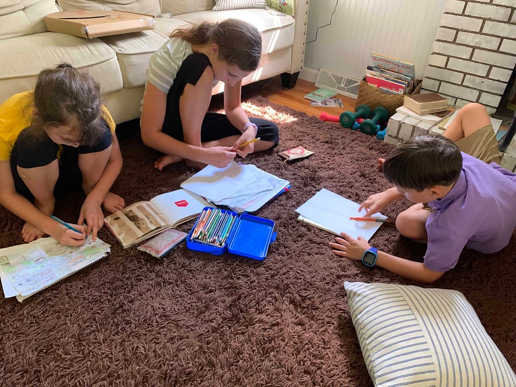 3 kids drawing together on the living room rug