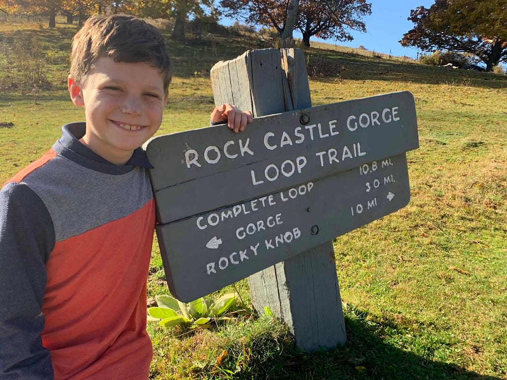 10 year old standing by the rock castle gorge loop trail sign before hiking it