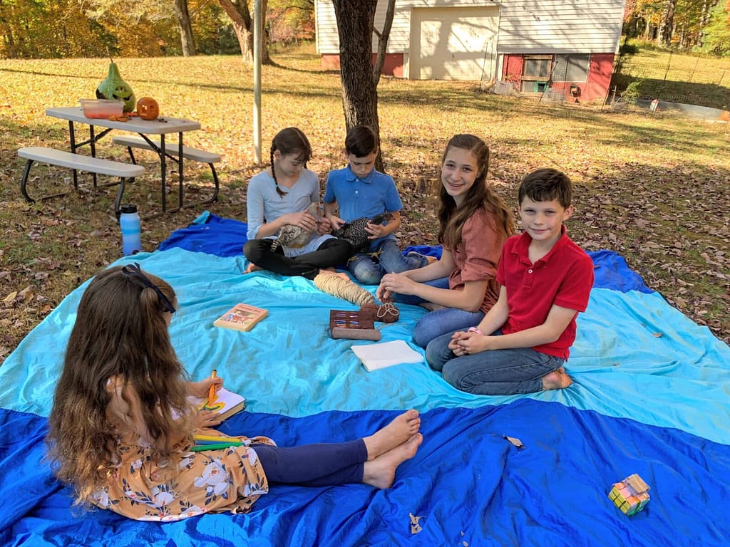 siblings sitting on a blue beach blanket in the shade in fall