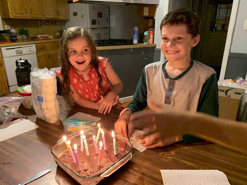 10 year old blowing out birthday candles with little sister watching and smiling