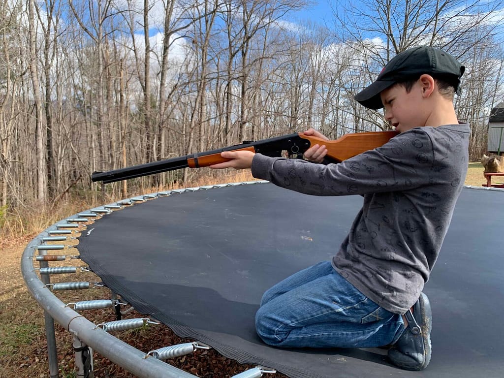 8 year old shooting a BB gun while on the trampoline