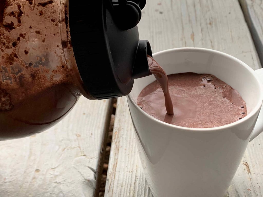 pouring raw milk hot chocolate from a jar into a white mug