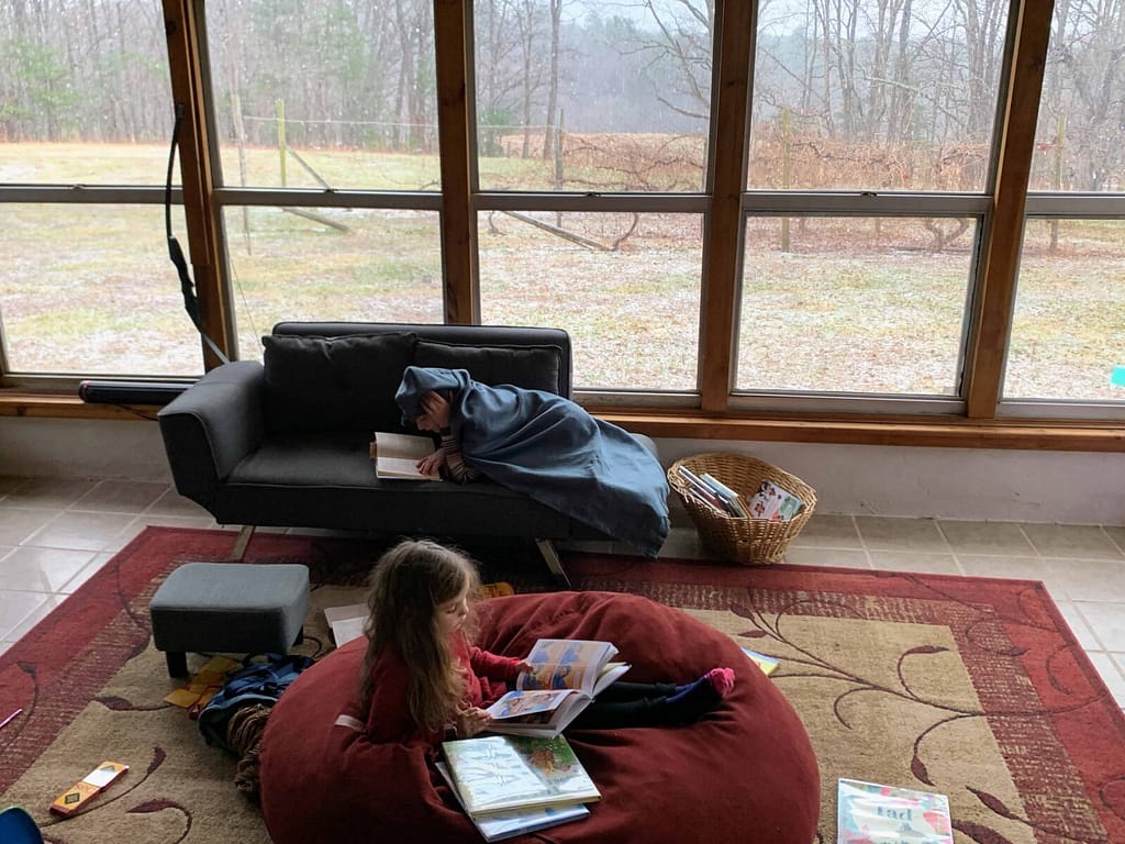 2 girls reading in a sunroom while watching it snow