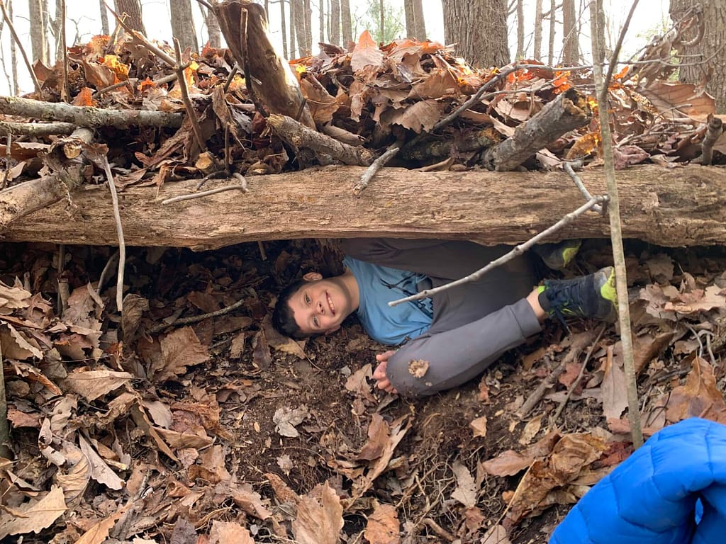 10 year old boy in a fort he made in the woods