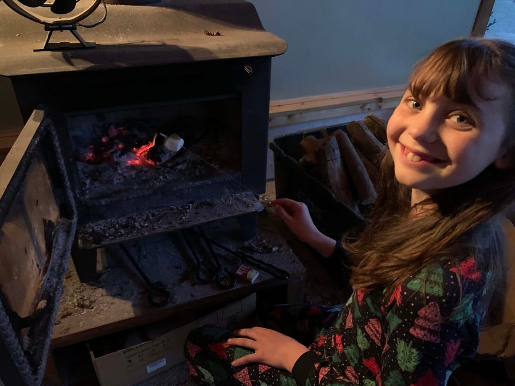 12 year old girl roasting marshmallows in a wood stove