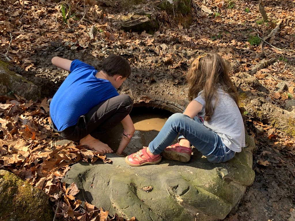 boy and girl getting leaves out of a tractor tire in the creek