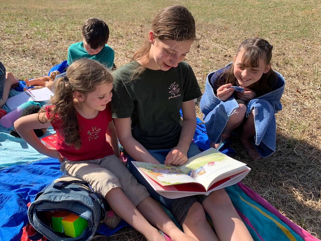 teen sister reading to her little sisters outside
