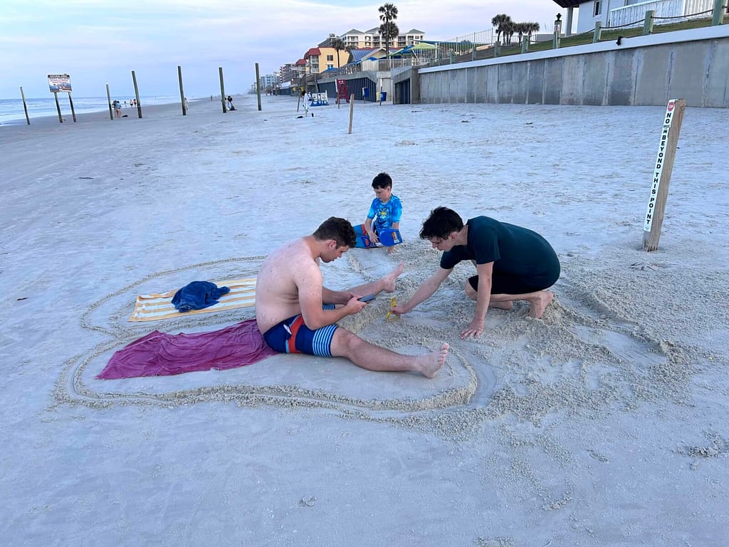 3 teen boys playing in the sand at the beach