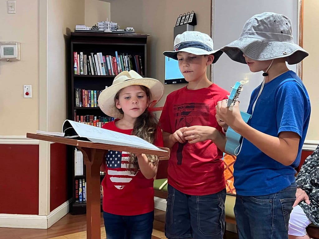 3 kids singing at a nursing home in patriotic clothing