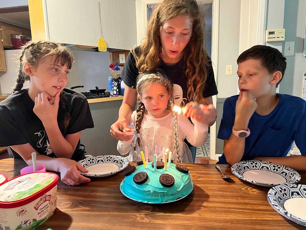 girl lighting her birthday candles with siblings watch