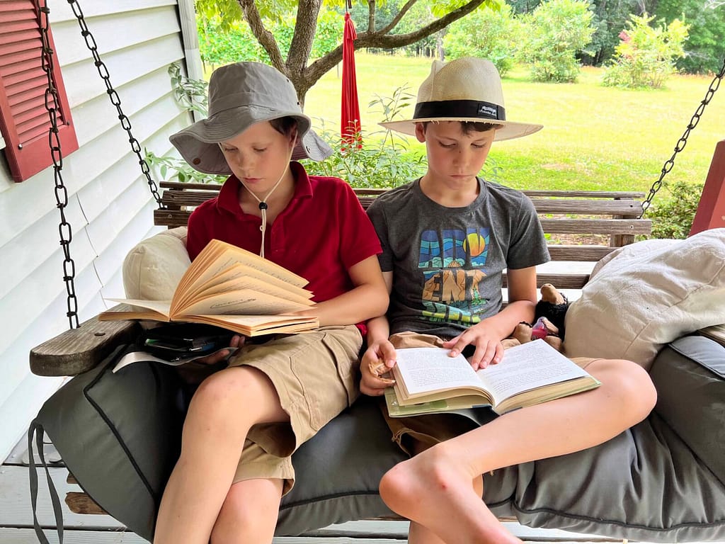 2 boys reading books on the porch swing