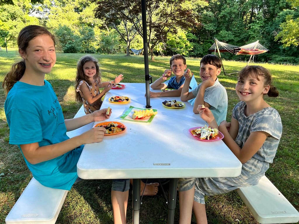 5 kids eating dinner at a picnic table
