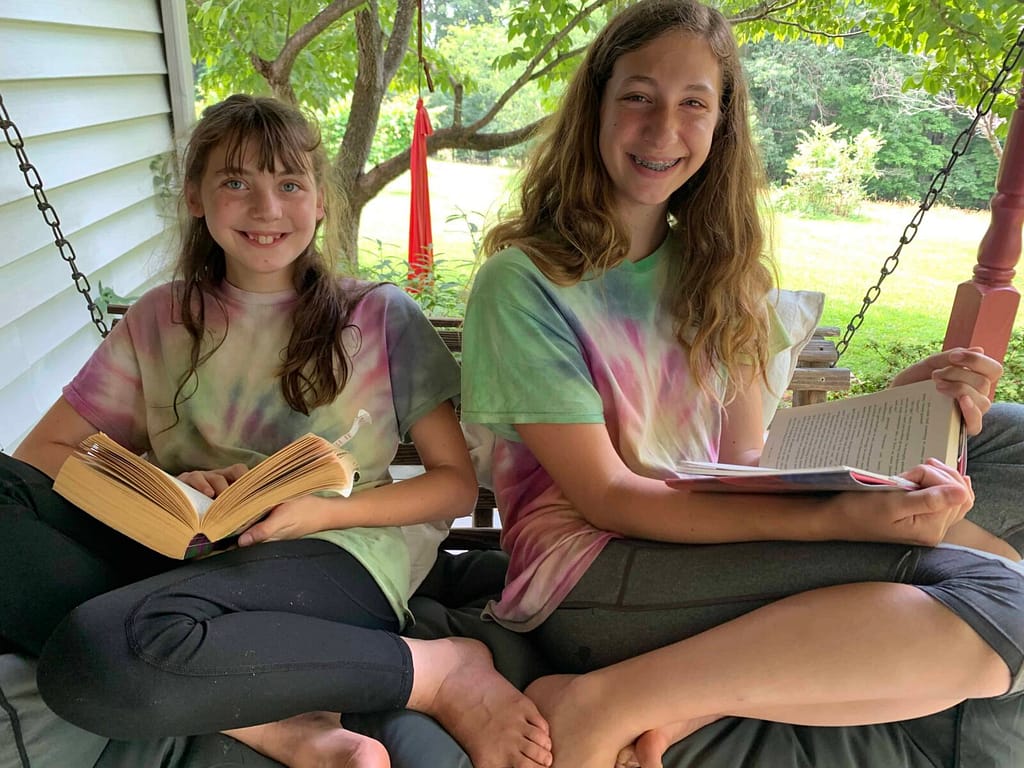 2 girls with tie dye shirts reading on a porch swing