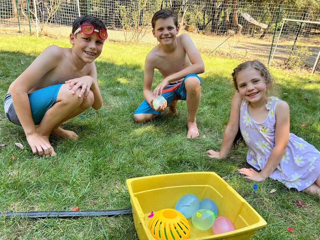 3 kids smiling by a bowl of waterballoons