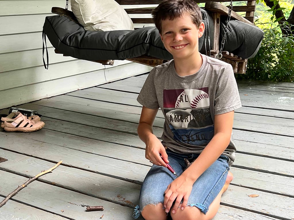 10 year old boy carving wands on the porch