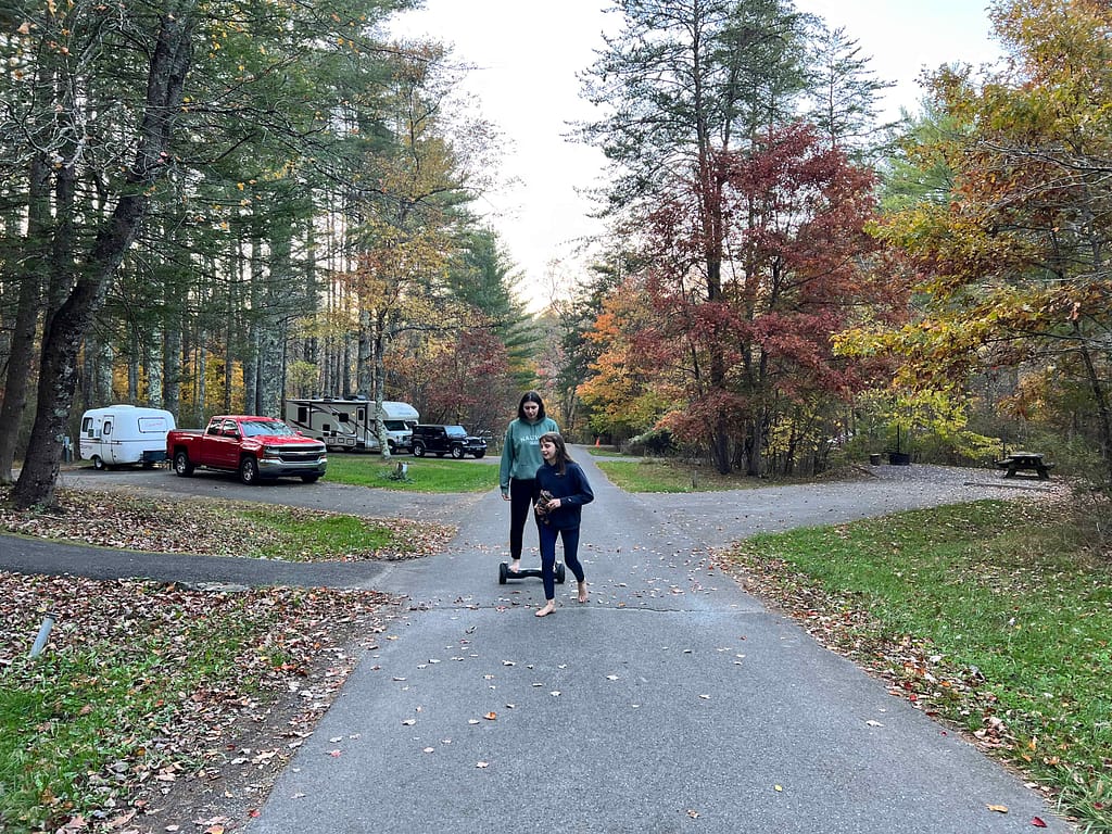 2 siblings riding a hoverboard at a campground in fall