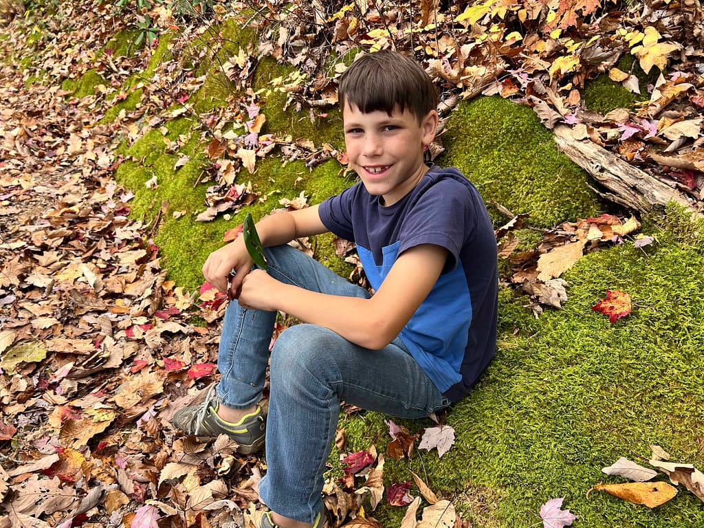 9 year old boy sitting on moss on a hike