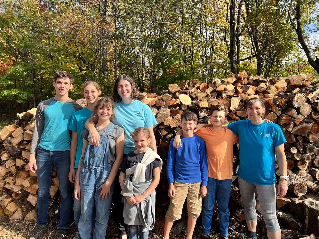 Family of 7 standing in front of a pile of wood they just stacked