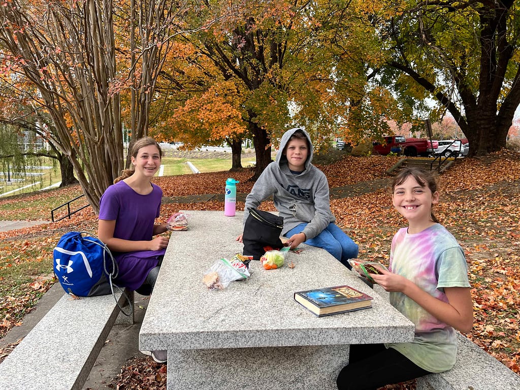 3 kids eating lunch at a picnic table