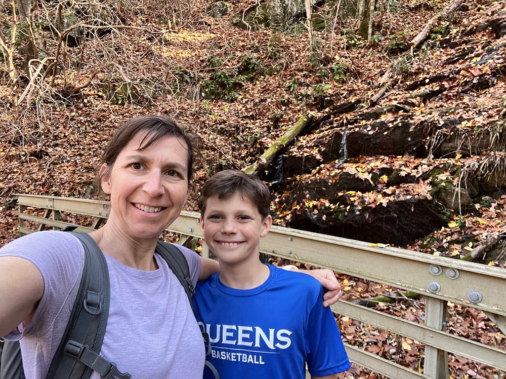 mom and son on bridge with waterfall and leaves behind them.