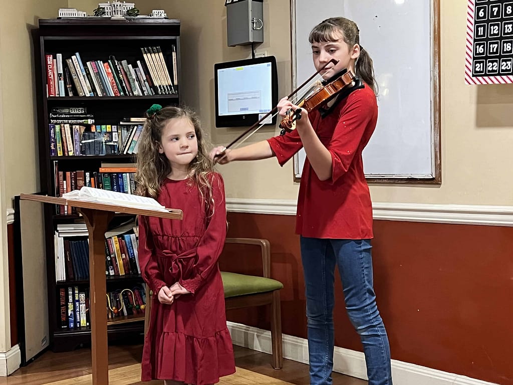 girl playing violin and her little sister watching