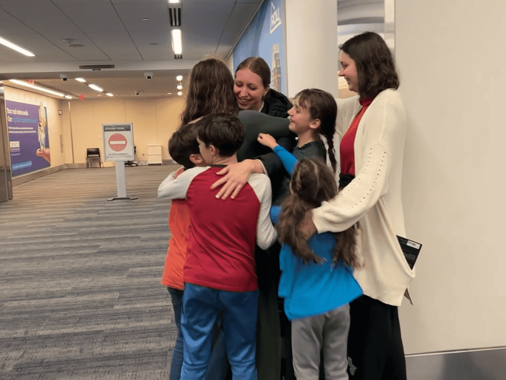 kids hugging sister as she gets off the airplane
