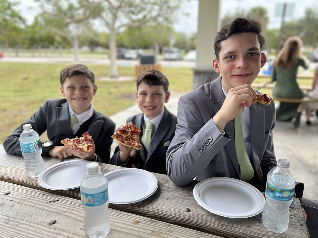 3 brothers in suits eating pizza at the park