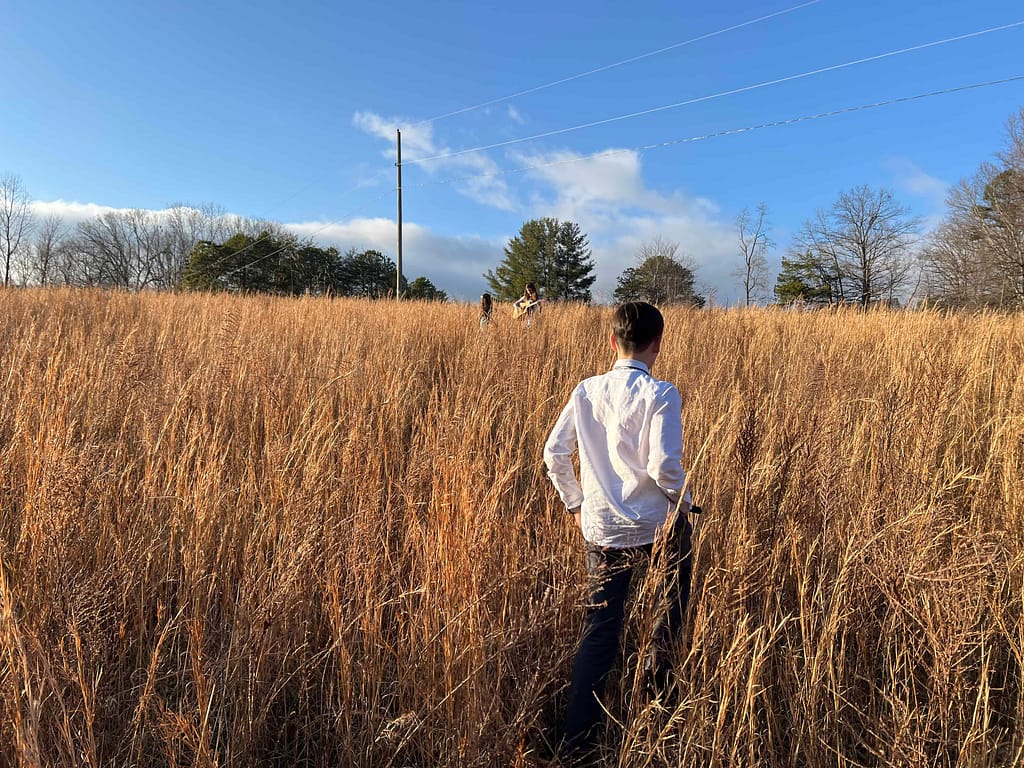boy walking through field of tall brown grass