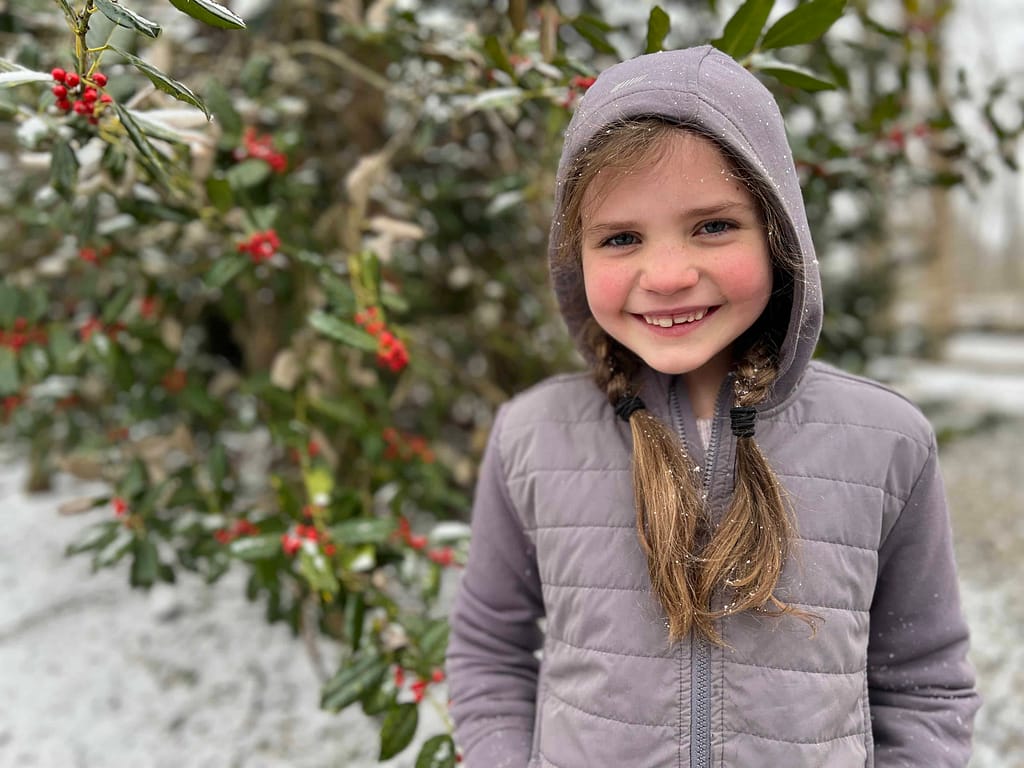7 year old girl standing in front of a snowy holly tree
